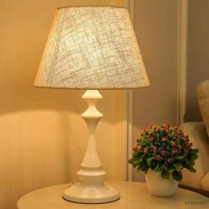 Biała lampa stołowa z lnianym abażurem i smukłą podstawą, widok z przodu